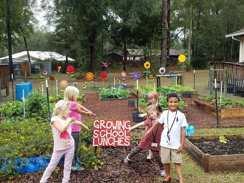 Newberry Elementary School's garden with kids pointing to "Growing for School Lunches" sign